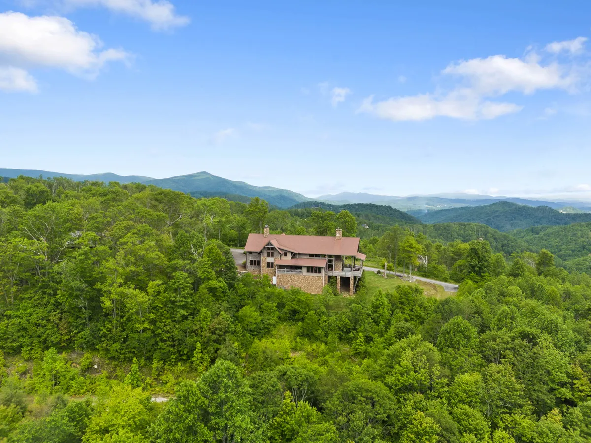 Featuring the home framed by tall trees and a vast mountain landscape in the background, this exterior image evokes a sense of tranquility and connection to nature. The porch and surrounding greenery offer a glimpse of the serene lifestyle available at the property.