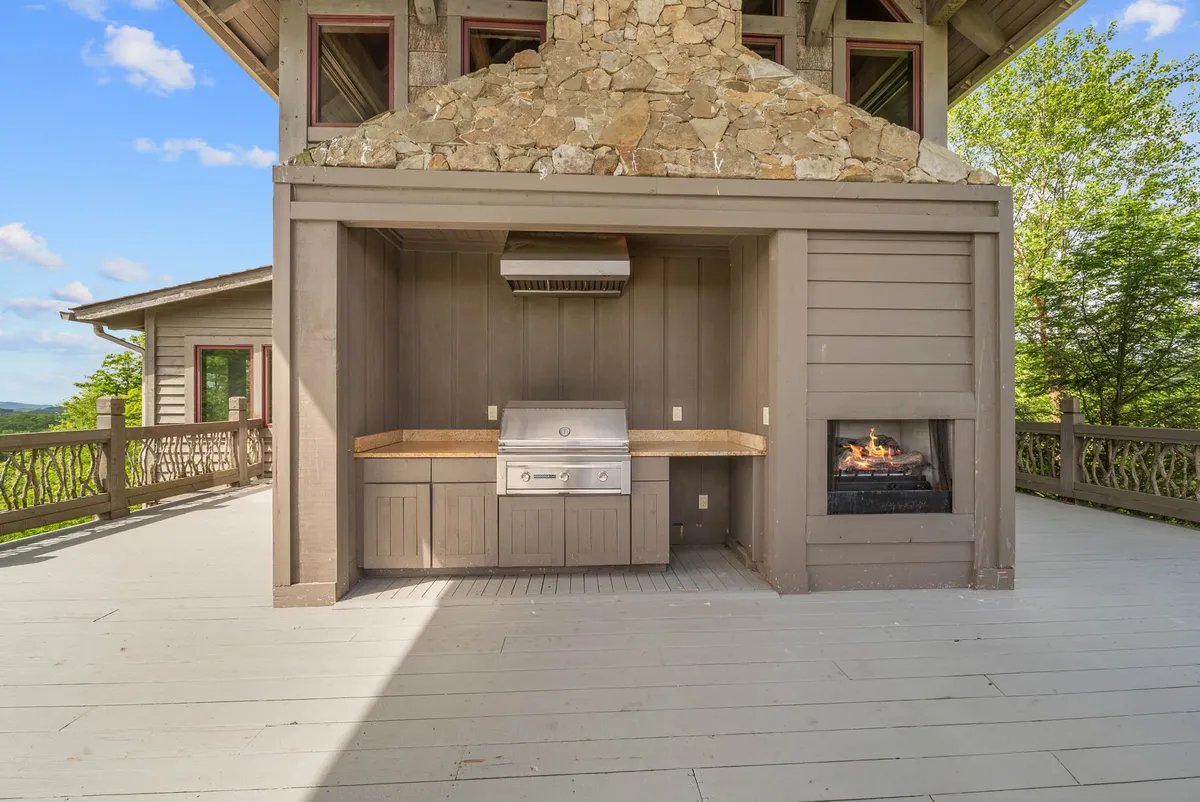 A lively outdoor living space featuring a fully equipped kitchen with a grill, a stone fireplace, and a spacious wooden deck. This inviting area overlooks the valley, ideal for sunset barbecues, winter evenings by the fire, and festive group celebrations.