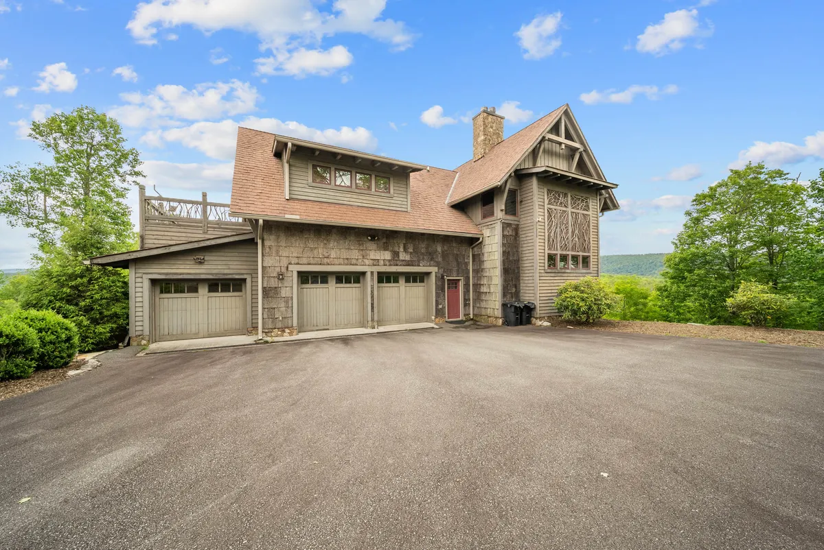 A striking exterior view of the home, showcasing its unique architectural design, the expansive driveway perfect for gatherings, abundant surrounding greenery, and a glimpse of the rooftop deck. The scene radiates a welcoming and serene atmosphere, suggesting space for family arrivals and outdoor celebration.