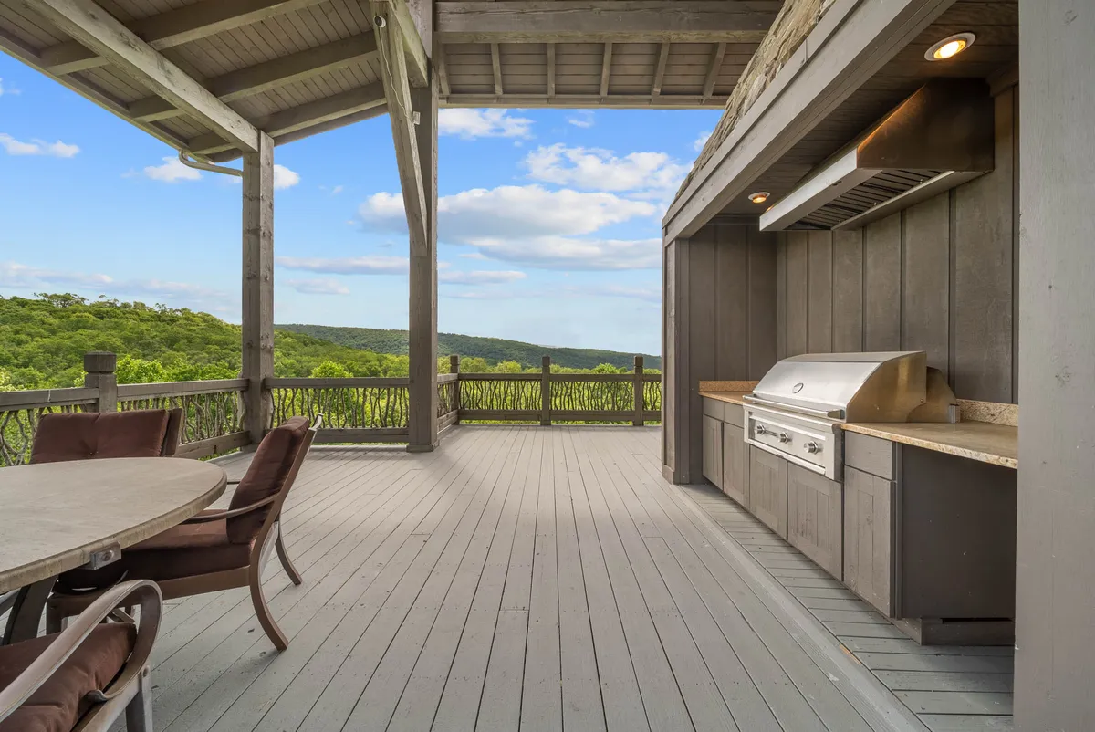 This exterior shot showcases a stylish outdoor kitchen and dining area set on a spacious deck with a sweeping panoramic view of the mountains. The modern grill, ample seating, and open-air ambiance highlight opportunities for outdoor entertaining and gourmet experiences in a luxurious setting.