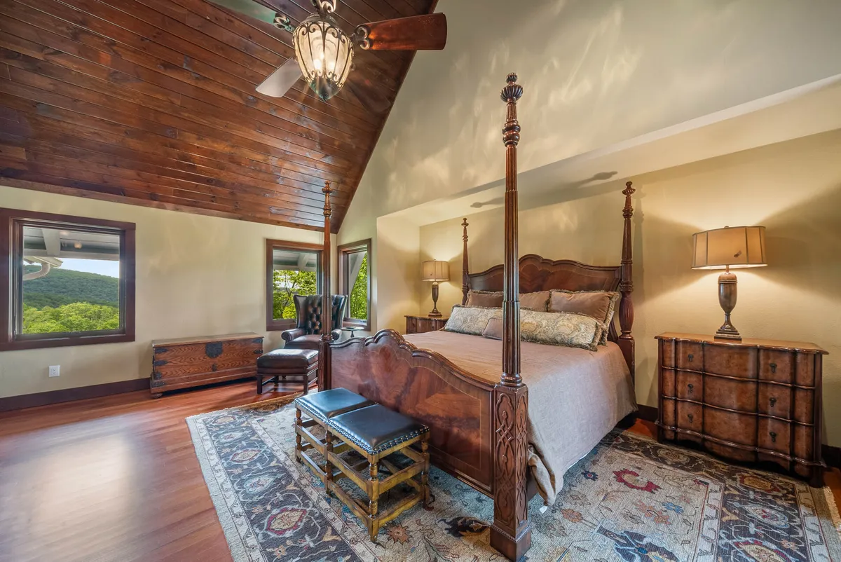 A tranquil king suite featuring a four-poster bed, ornate chandelier, wooden ceiling, and large windows that overlook the landscape. The room is elegantly decorated with cozy furnishings and hints of mountain-inspired decor, creating a restful and private retreat.