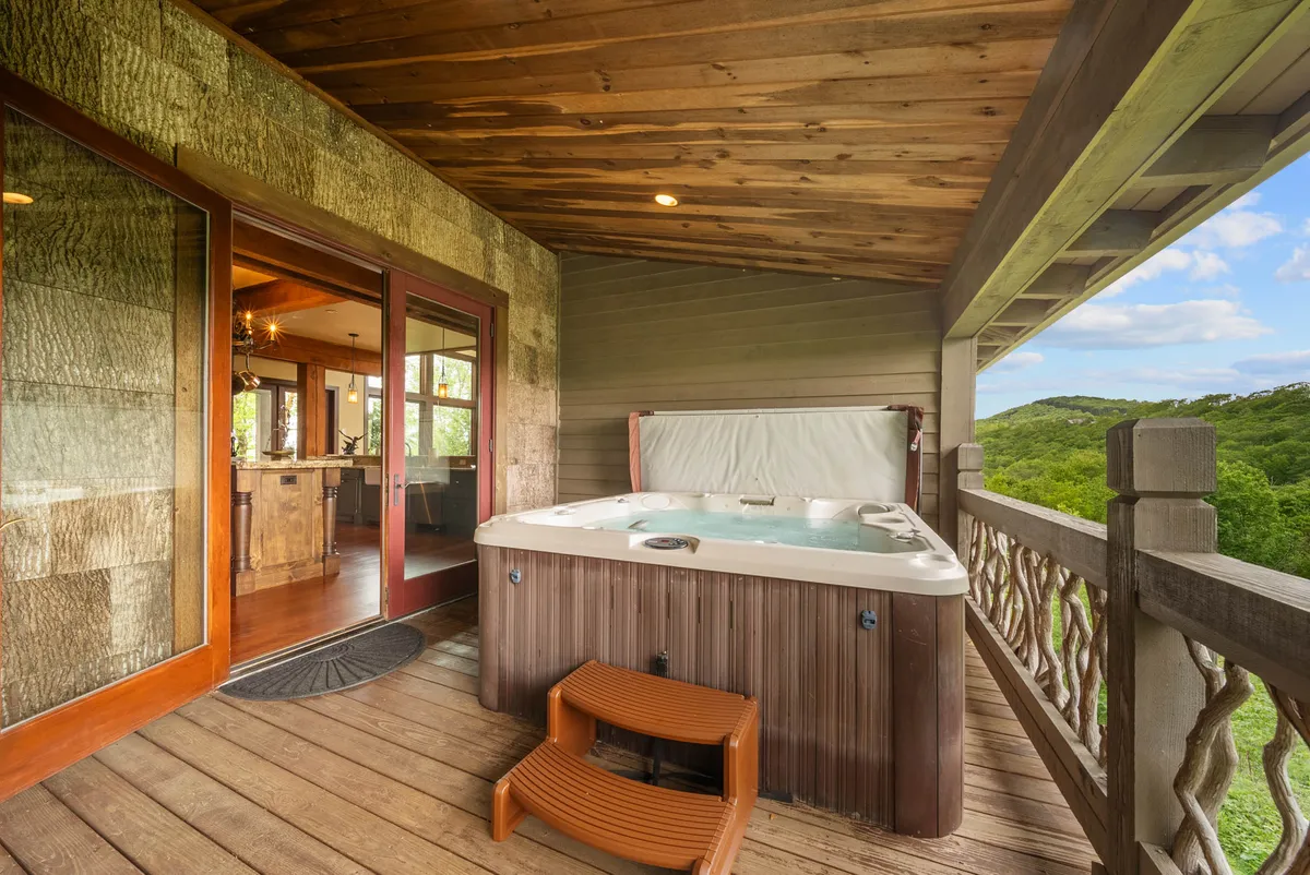 A serene exterior image showing a modern hot tub nestled on a wooden deck with sweeping views of rolling hills and lush greenery. The setup is ideal for relaxation, socializing, and soaking in the mountain scenery, whether under the stars or in the morning light.